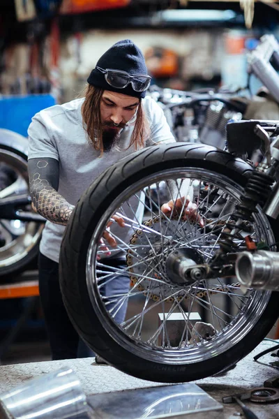 ガレージ バイクをカスタマイズして修復壊れたホイール機構で働く現代の刺青の男の肖像 — ストック写真