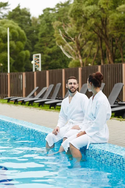 Giovane Coppia Seduta Bordo Piscina Con Gambe Acqua Parlando Resort — Foto Stock