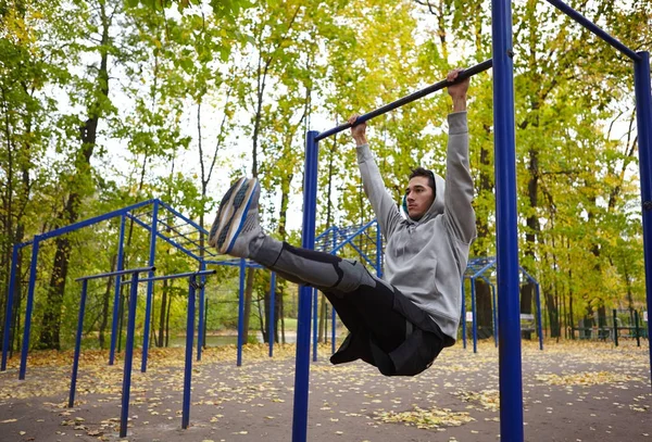 秋の公園 全身肖像画でワークアウト中鉄棒で懸垂をしている自信を持って若いスポーツマン — ストック写真