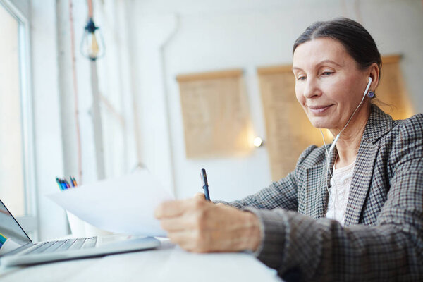 Aged female listening to music in earphones while reading paper