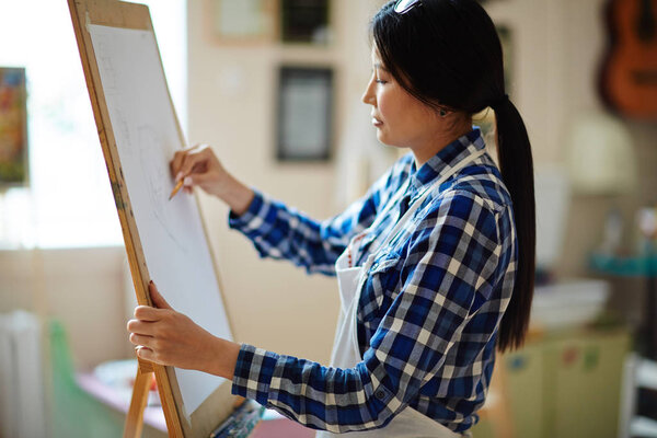 Young girl drawing on paper with pencil in studio of arts