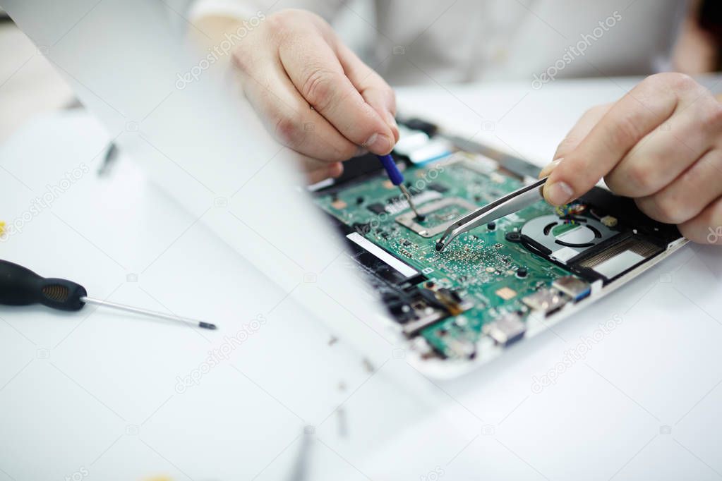 Closeup shot of male hands repairing parts in disassembled laptop using screwdriver and different tools on table in workshop