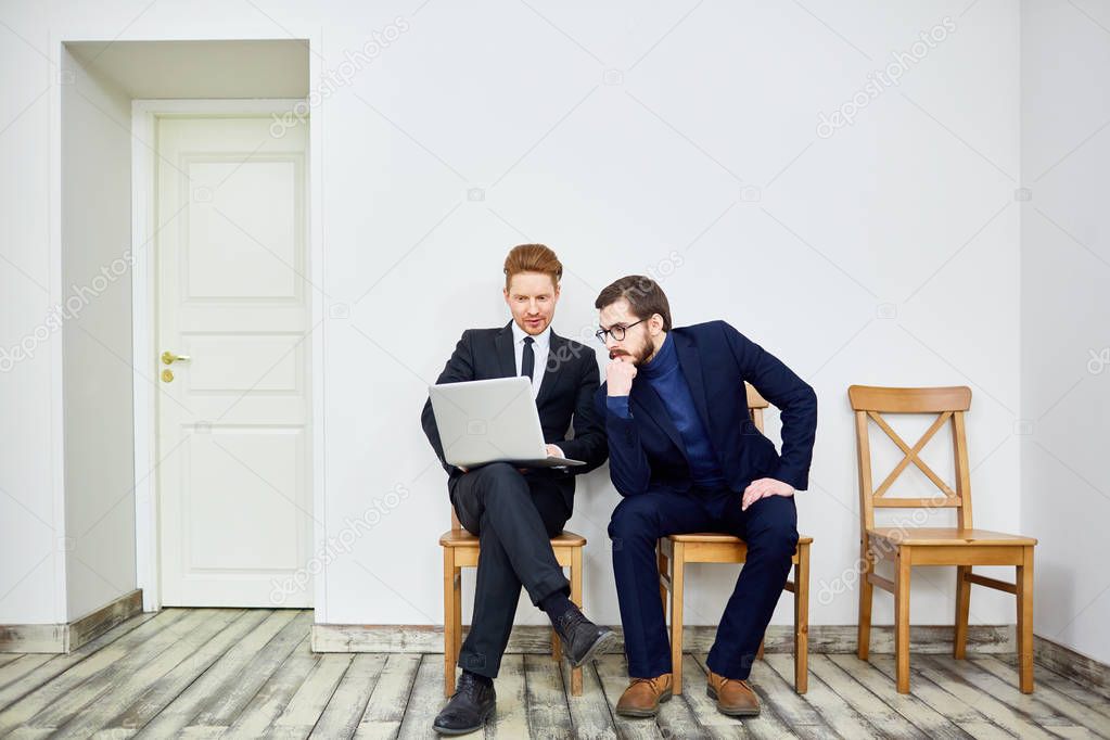 Portrait of two business people using laptop sitting on chairs in waiting room outside office