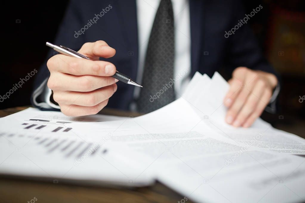 Closeup portrait of unrecognizable successful businessman wearing black formal suit reviewing finance graphs and signing papers and work desk