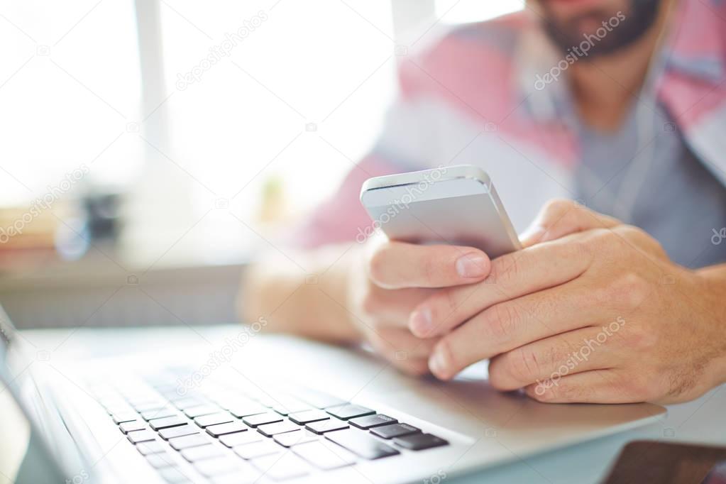 Close-up of businessman planning his day with smartphone app, he sitting at table in front of laptop
