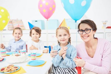 Bir doğum günü şapkalı kız şenlikli masaya otururken kucaklayan anaokulu öğretmeni