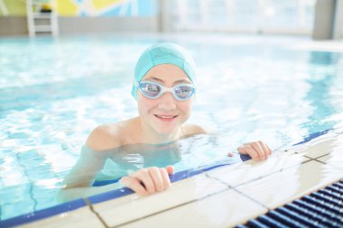 Yüzme-kap ve Yüzme Havuzu saf suda ayakta gözlük genç yüzücü