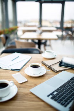 Üç bardak koyu siyah kahve, belgeler, not defteri ve becerikli alet Cafe ahşap masa üstünde