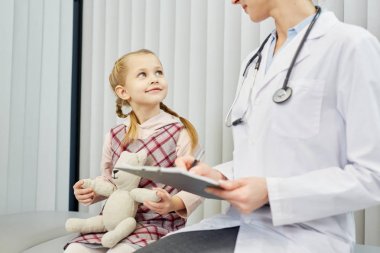 Kliniklerde onun doktorun tavsiyesi dinlerken teddybear mutlu küçük kız