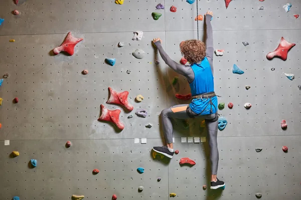 若いスポーツマンのタイト ロープにぶら下がっているクライミングの壁の背面図 — ストック写真