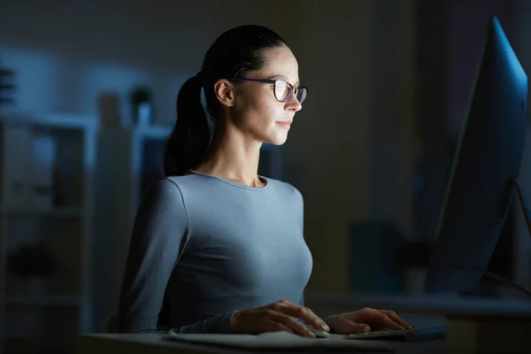 暗いオフィスでコンピューター モニターの前に彼女の職場で座っている若い女性 — ストック写真