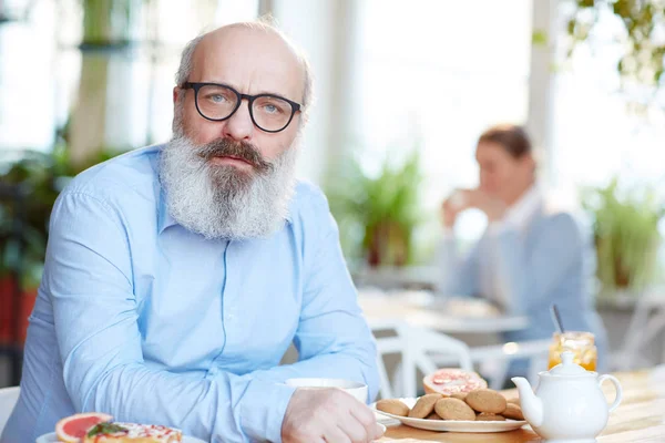 长着灰色胡子的老人在咖啡馆里花时间看相机 — 图库照片