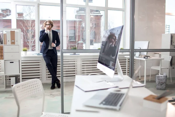 Joven Hombre Negocios Elegante Traje Pie Junto Ventana Oficina Hablando —  Fotos de Stock