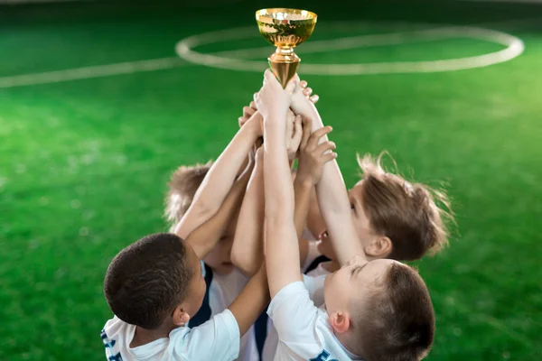 Group of young football champions raising hands with gold award