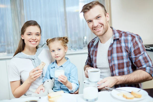 年轻迷人的已婚夫妇和他们可爱的小女儿喝着饼干的桌子 — 图库照片