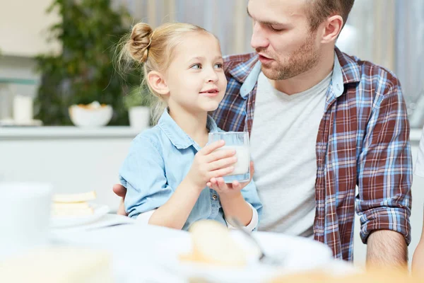 朝食で牛乳のガラスと彼のかわいい小さな娘に話している若い父親 — ストック写真