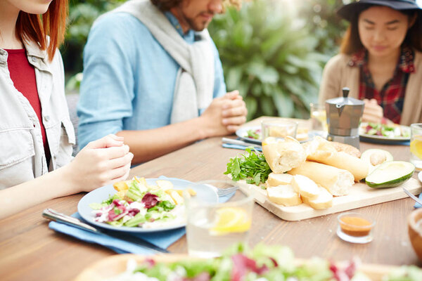 Стол с домашней едой и руками нескольких друзей, молящихся перед ужином
