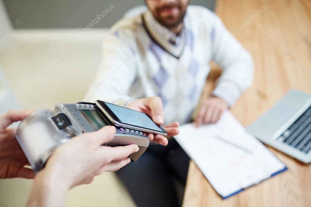 Mobile man holding his smartphone close to payment machine in hands of waitress