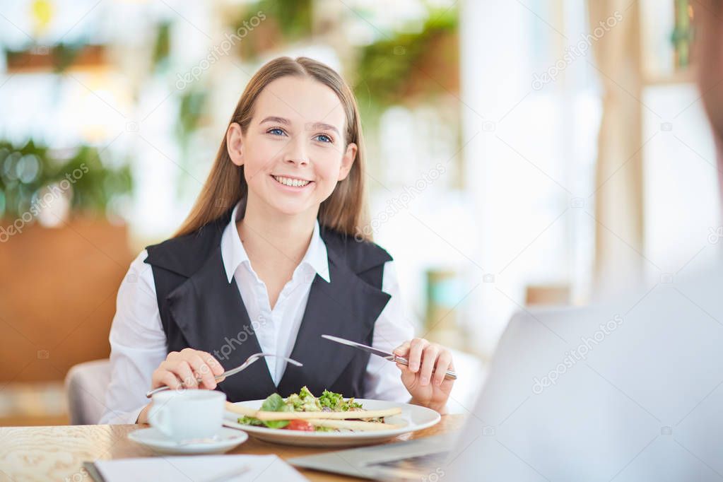 Young manager with toothy smile looking at colleague during talk by business lunch in cafe
