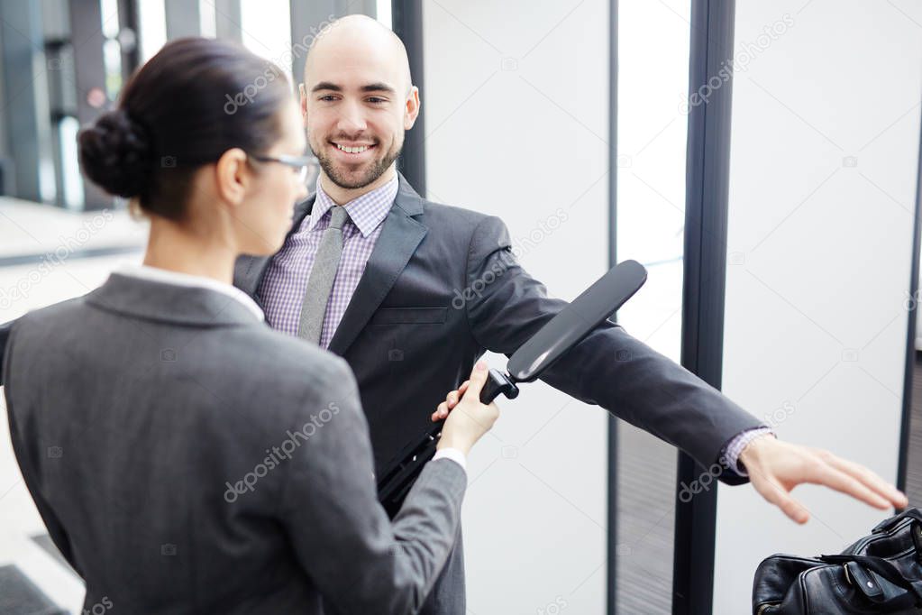 Smiling businessman looking at young airport security scanning his arm by entrance