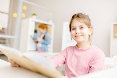 Kopma sınıfta otururken kameraya bakıyor kitap ile küçük okuyucu