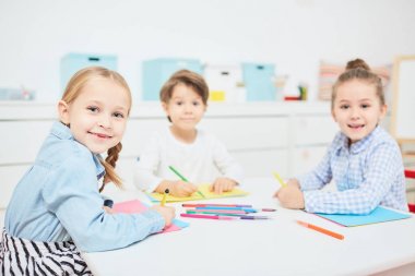 Mutlu küçük kız ve erkek Anaokulunda ders çizim, kamera bakıyor