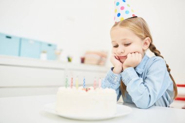 Üzgün küçük kızın doğum günü Cap şenlikli Pastaya mumları ile seyir