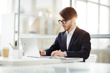 Dizüstü bilgisayar masası tarafından oturan ve webinar ya da online iş toplantısında izlerken genç emin iş adamı