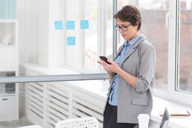 İşkadını ofis pencere tarafından dururken çıkıyor smartphone ile