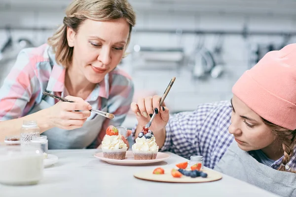 两个年轻的专业 Foodstylists 把釉上的浆果 而工作超过装饰的蛋糕 — 图库照片