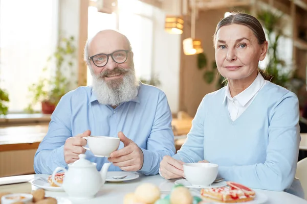 Happy mature man and woman looking at camera while spending time in cafe by dessert