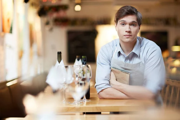 年轻的当代服务员倚着桌子看着咖啡馆里的照相机 — 图库照片