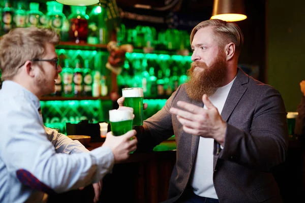 两个友好的男子与啤酒坐在酒吧柜台在酒吧和讨论新闻 — 图库照片