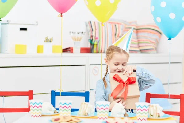 Kind Geburtstagskappe Öffnet Geschenkbox Und Betrachtet Ihr Geschenk Festlichen Tisch — Stockfoto