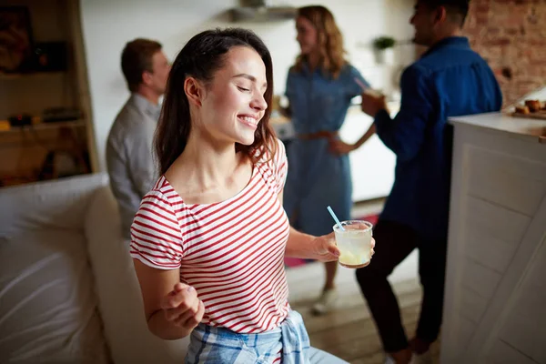 Young woman with drink enjoying home party with her friends talking on background