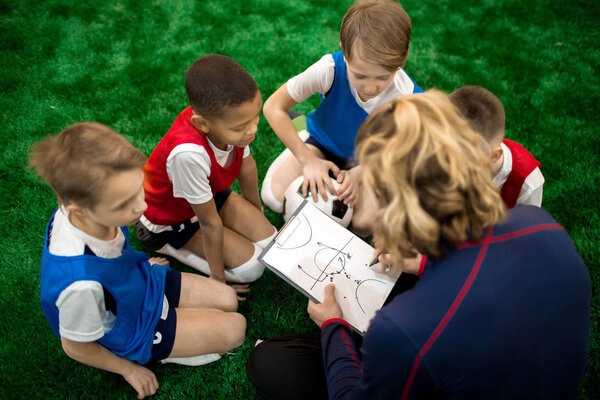 Football instructor drawing scheme of moving during soccer game or training and explaining it to group of boys