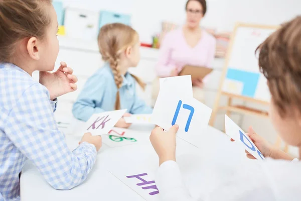 幼稚園でのレッスンの時に先生に聞いて 英語の文字と紙のカードといくつかの小さな子供 — ストック写真