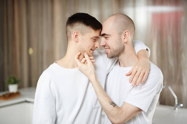 Amorous homosexual couple in embrace cuddling at home
