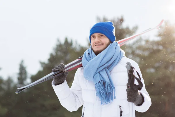 白い冬ジャケット 青のスカーフ ビーニー帽子組のスキーを押しながら冬の公園で時間を過ごす若いスポーツマン — ストック写真