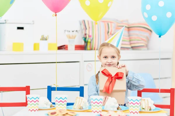 かわいい女の子彼女の誕生日パーティーに役立ったテーブルに坐っている間ギフト ボックスを開く — ストック写真