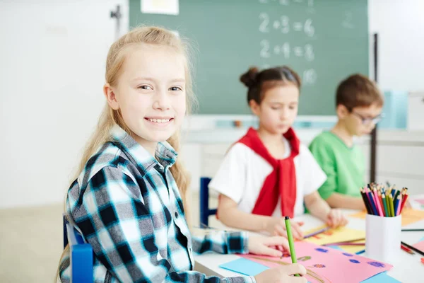 Feliz Colegiala Rubia Sonriéndote Sentada Junto Escritorio Dibujando Lección — Foto de Stock