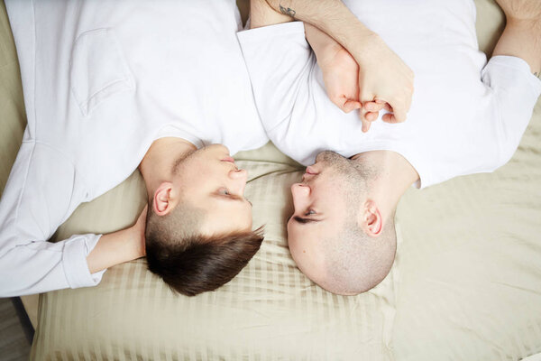Overview of young gay men looking at one another with their heads on pillow