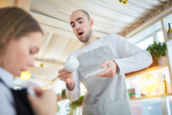 Careless waiter trying to catch cup of tea while young woman looking if there is stain on her clothes