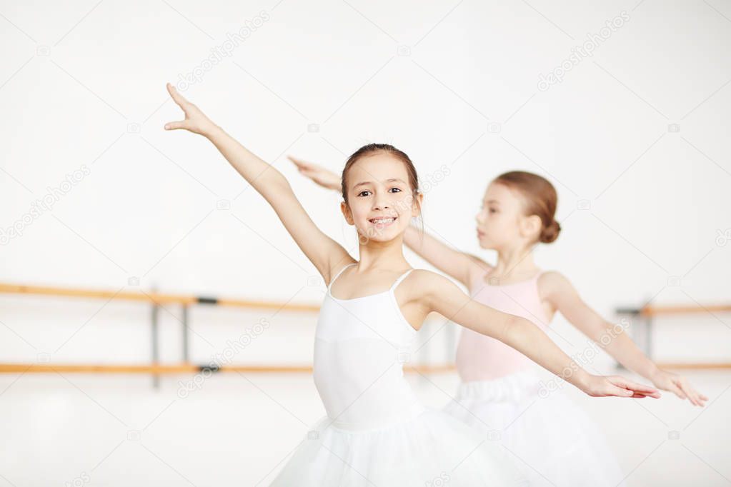 Two little girls outstretching arms while training in ballet class