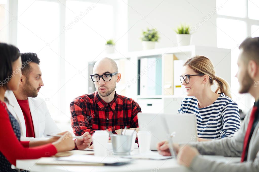 Serious young man looking at one of colleagues at meeting during working discussion