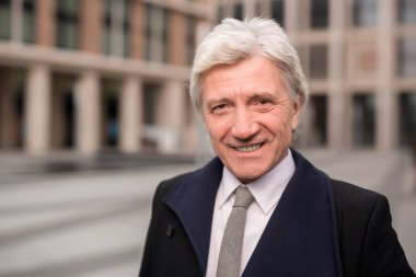 Siyah palto ve gri kravat gülümseme ile açık havada kameraya bakarak zarif olgun adam