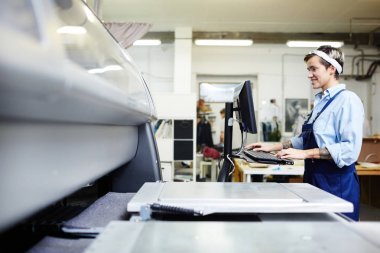 Genç grafik tipografi işçi Tekdüzen Bilgisayar Monitörü önünde duran ve yazdırma için örnek seçme