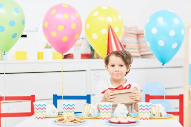 Cap holding paket ile mevcut şenlikli masaya otururken doğum günü çocuğu