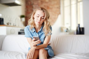 Genç kadın evde kanepede oturan ve onun smartphone içinde mesajlaşma