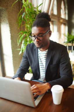 Masasının önünde dizüstü bilgisayar ve ağ kafede oturan genç Afro-Amerikan Yöneticisi